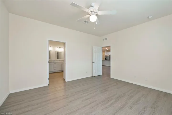 Unfurnished bedroom featuring light wood-style floors, ensuite bath, and ceiling fan