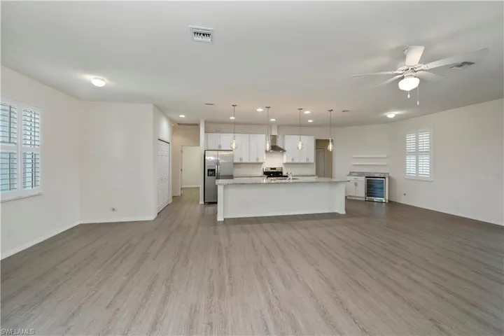 Kitchen with open floor plan, a ceiling fan, white cabinetry, appliances with stainless steel finishes, and wine cooler