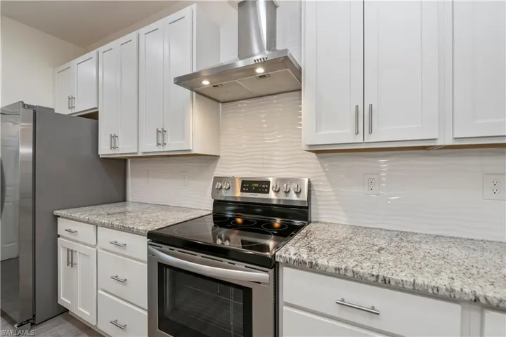 Kitchen with stainless steel appliances, wall chimney exhaust hood, white cabinets, and tasteful backsplash