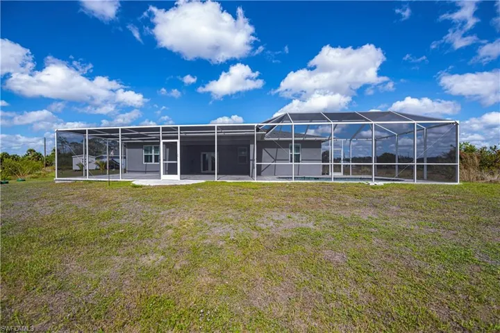 Back of house with a yard, glass enclosure, and a patio
