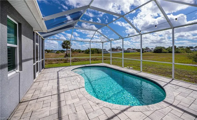 Outdoor pool with a patio, glass enclosure, and a yard