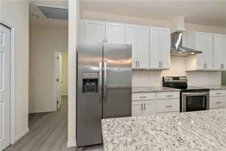 Kitchen with stainless steel appliances, wall chimney range hood, backsplash, light wood finished floors, and light stone countertops