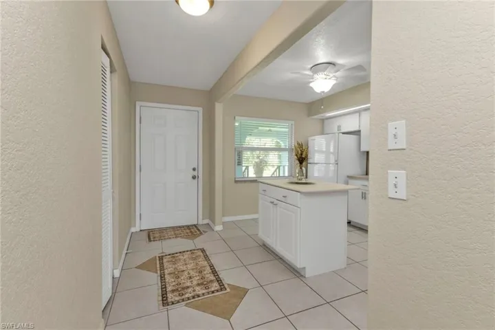 Kitchen with a center island, light tile patterned floors, a textured ceiling, white cabinets, and white refrigerator