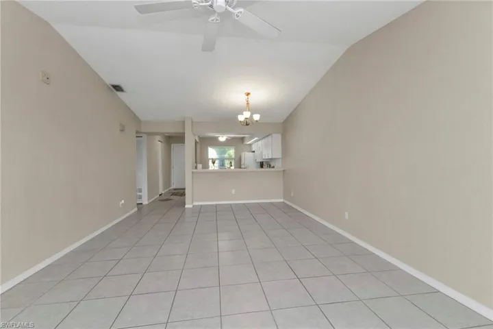 Unfurnished living room featuring light tile patterned floors, vaulted ceiling, and ceiling fan with notable chandelier
