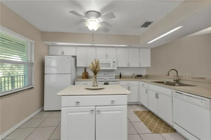Kitchen with white cabinetry, sink, white appliances, and light tile patterned floors
