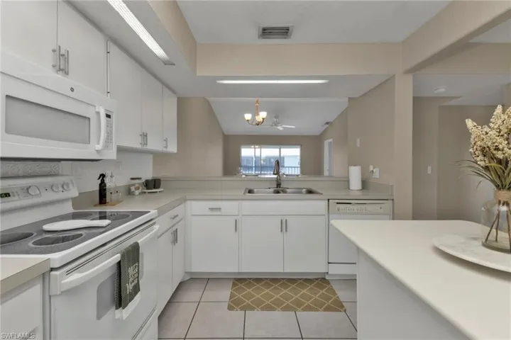 Kitchen featuring white cabinetry, white appliances, lofted ceiling, a chandelier, and sink