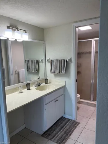 Bathroom with vanity, walk in shower, toilet, tile patterned floors, and a textured ceiling