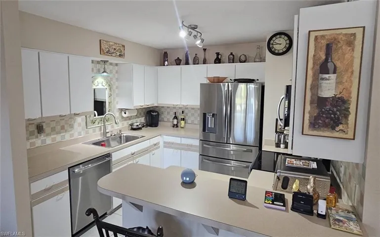 Kitchen featuring a peninsula, decorative backsplash, stainless steel appliances, light countertops, and white cabinetry