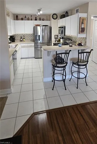Kitchen with a kitchen bar, stainless steel appliances, light countertops, backsplash, and white cabinetry