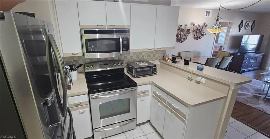 Kitchen with a peninsula, stainless steel appliances, light countertops, white cabinets, and backsplash