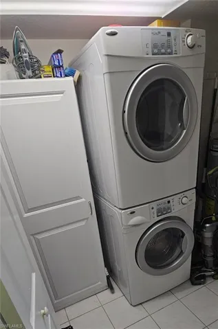 Laundry area with stacked washer / drying machine and light tile patterned flooring