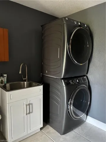 Washroom featuring light tile patterned flooring, stacked washer and clothes dryer, cabinet space, and a textured ceiling