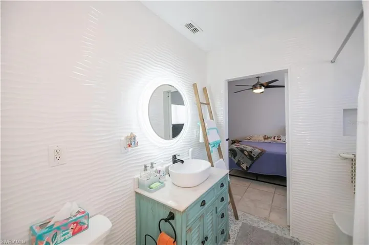Ensuite bathroom featuring vanity, light tile patterned floors, and ceiling fan