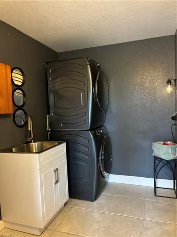 Laundry room featuring estacked washer and dryer, cabinet space, a textured ceiling, and light tile patterned floors
