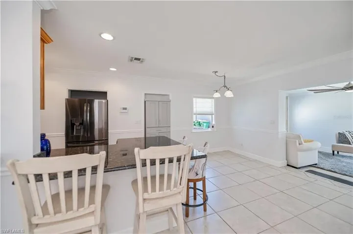 Kitchen with a breakfast bar, stainless steel fridge with ice dispenser, light tile patterned flooring, dark stone counters, and ornamental molding