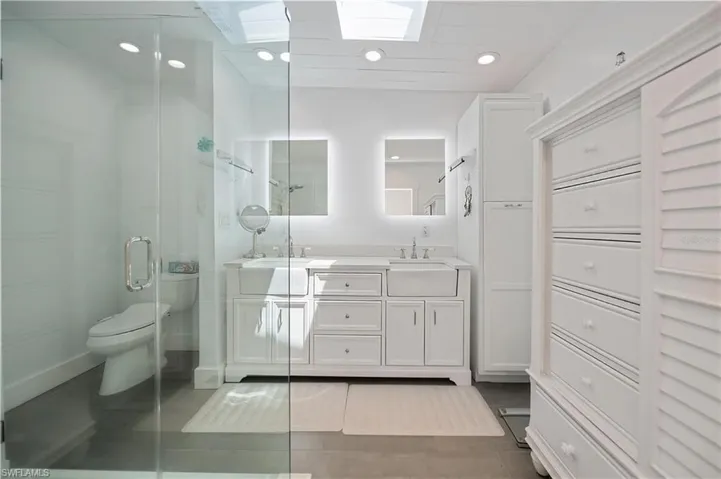 Bathroom featuring a skylight, a shower stall, double vanity, recessed lighting, and light tile patterned flooring