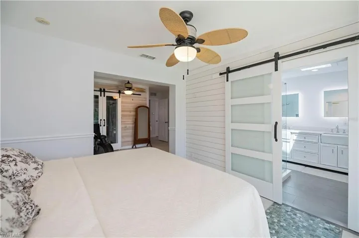 Bedroom with a barn door, connected bathroom, a ceiling fan, wood walls, and arched walkways