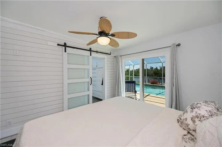 Bedroom featuring access to exterior, wood walls, a barn door, a ceiling fan, and a water view