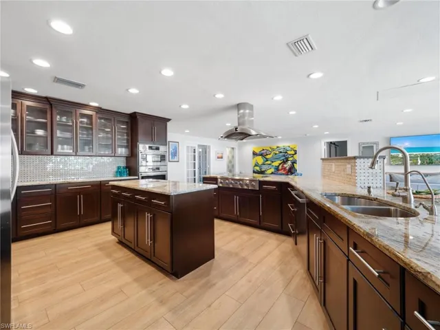 Kitchen featuring a kitchen island, tasteful backsplash, glass fronted cabinets, light stone counters, and recessed lighting