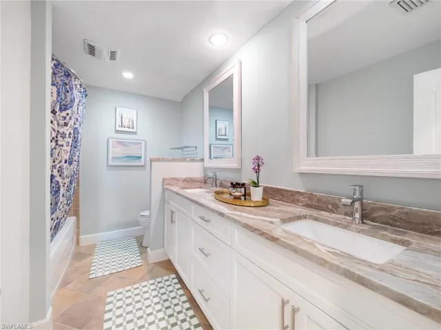 Bathroom with double vanity, shower / bathtub combination with curtain, light tile patterned floors, and recessed lighting