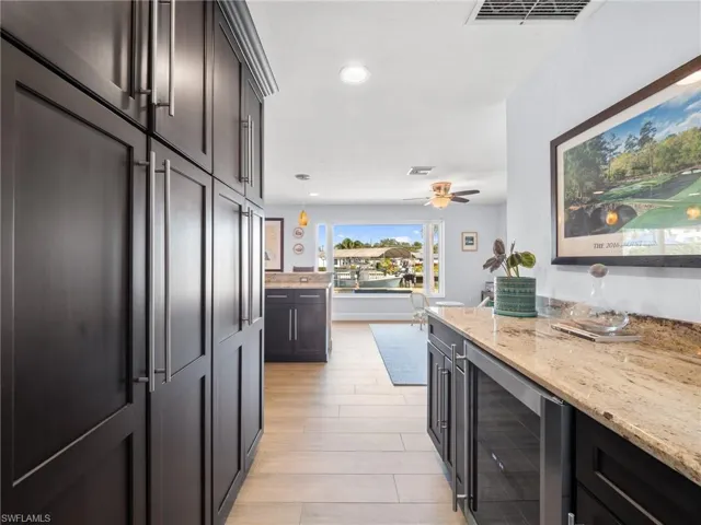 Kitchen featuring wine cooler, light stone counters, pendant lighting, light wood finished floors, and ceiling fan