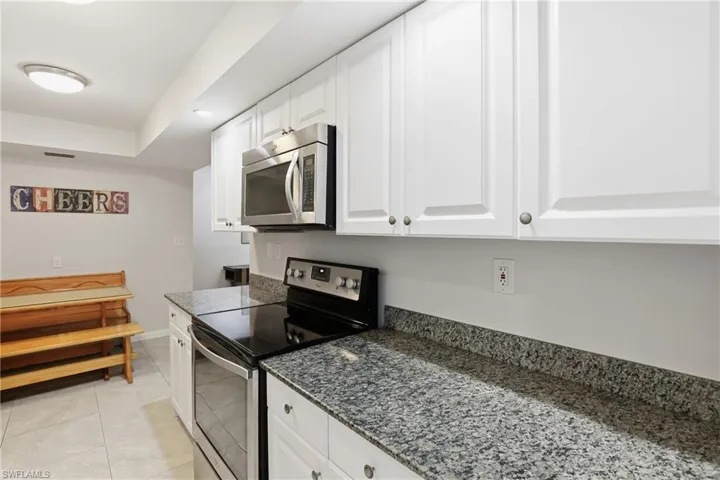 Kitchen with stainless steel appliances, dark stone counters, white cabinets, light tile patterned floors, and recessed lighting