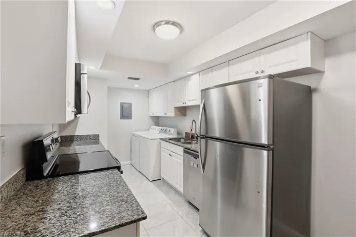 Kitchen featuring stainless steel appliances, white cabinetry, light tile patterned floors, dark stone counters, and recessed lighting