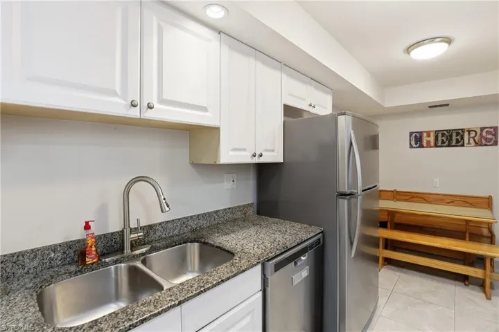 Kitchen with appliances with stainless steel finishes, white cabinets, light tile patterned floors, and dark stone counters