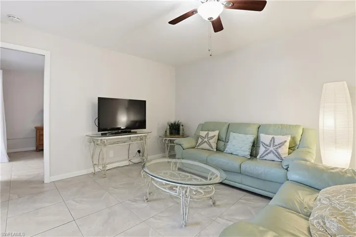 Tiled living room with a ceiling fan and baseboards