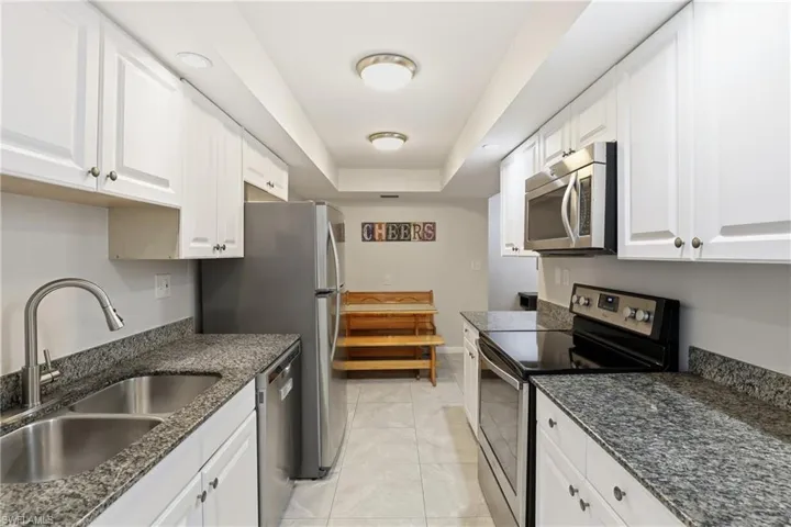Kitchen featuring appliances with stainless steel finishes, a tray ceiling, dark stone countertops, and white cabinets