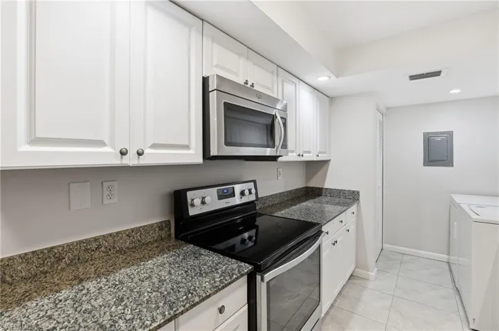 Kitchen with appliances with stainless steel finishes, white cabinetry, recessed lighting, electric panel, and dark stone countertops