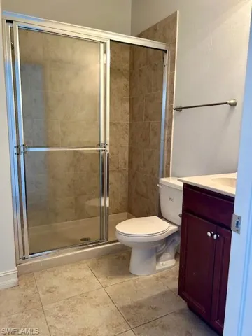 Bathroom featuring a glass-enclosed shower with tile surround, a single vanity with a white countertop and dark wood-finish cabinetry, and neutral-toned tile flooring