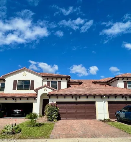 Mediterranean-inspired residence featuring a terracotta tile roof, stucco exterior, multiple attached garages with wood-finish doors, and paver driveway