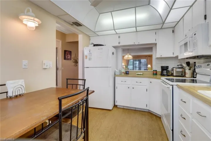 Kitchen featuring unique lighting, white appliances & cabinetry, tasteful backsplash, and light wood-style floors