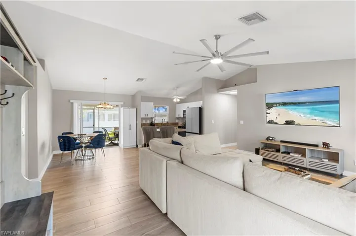Living room with light wood-style floors, vaulted ceiling, ceiling fan, and a chandelier