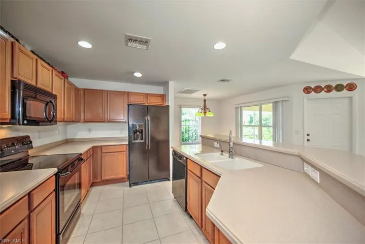 Kitchen with black appliances, sink, light tile floors, and pendant lighting