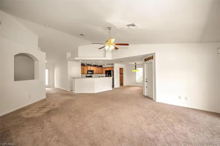 Great room room featuring light colored carpet, high vaulted ceiling, and ceiling fan