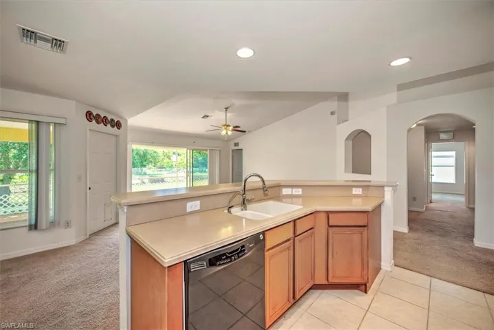 Kitchen featuring light tile floors, black dishwasher, sink, ceiling fan, and vaulted ceiling