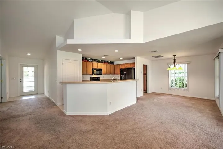 Kitchen with black appliances, decorative light fixtures, a towering ceiling, a notable chandelier, and light colored carpet
