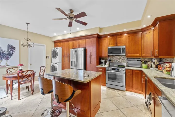 Kitchen with light stone countertops, stainless steel appliances, pendant lighting, a center island, and stacked washer and clothes dryer