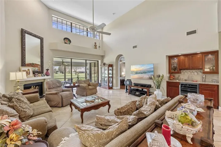 Living room with a towering ceiling, ceiling fan, indoor bar, beverage cooler, and light tile patterned floors