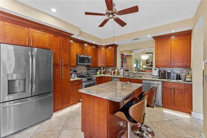 Kitchen featuring decorative backsplash, a breakfast bar area, appliances with stainless steel finishes, light stone countertops, and pendant lighting