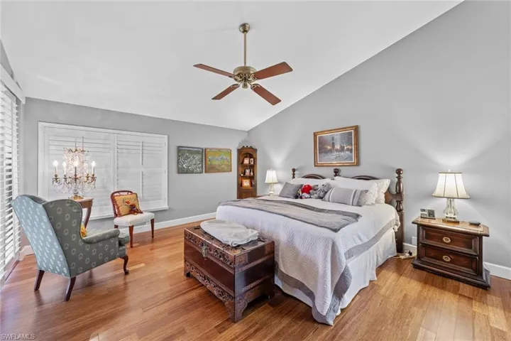 Bedroom with vaulted ceiling, light hardwood / wood-style flooring, and ceiling fan with notable chandelier