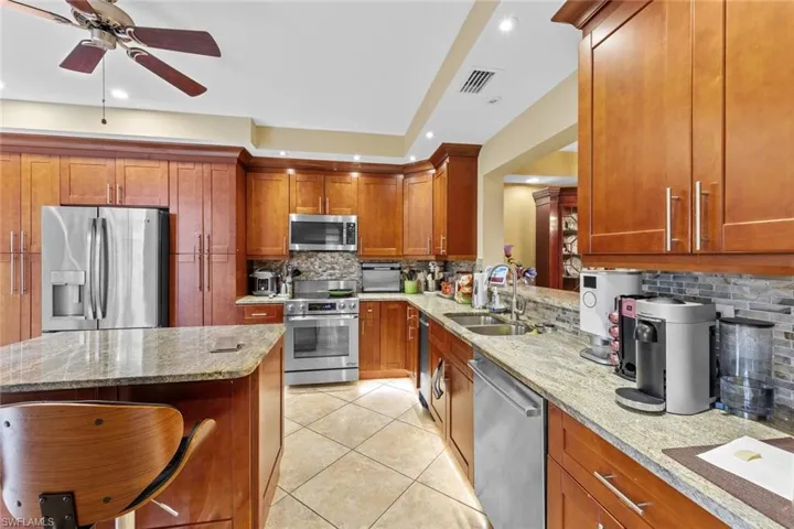 Kitchen featuring decorative backsplash, sink, light tile patterned floors, appliances with stainless steel finishes, and light stone counters
