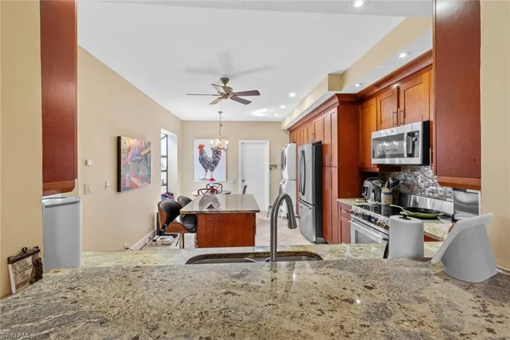 Kitchen with kitchen peninsula, backsplash, sink, appliances with stainless steel finishes, and light stone counters