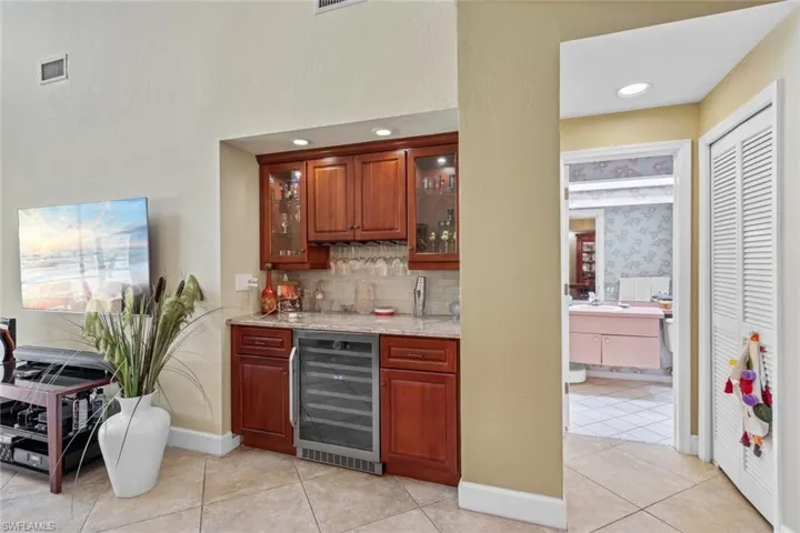 Bar featuring wine cooler, light tile patterned floors, backsplash, sink, and light stone counters