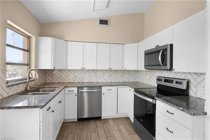 Kitchen with stainless steel appliances, dark stone counters, lofted ceiling, white cabinets, and wood finish floors