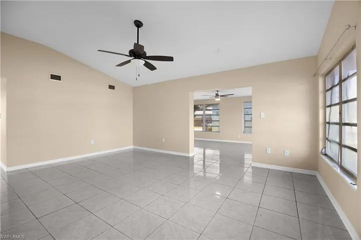 Empty room featuring light tile patterned floors, vaulted ceiling, and ceiling fan