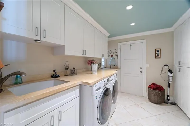 Laundry room featuring crown molding, washing machine and dryer, light tile patterned floors, cabinet space, and a sink
