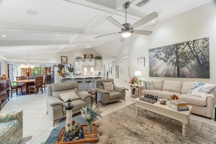 Living room with light tile patterned floors, visible vents, coffered ceiling, lofted ceiling with beams, and ceiling fan with notable chandelier